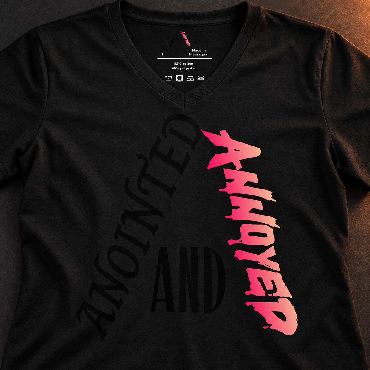 Anointed and Annoyed black V-neck tee detail with tonal black lettering and pink-to-peach print